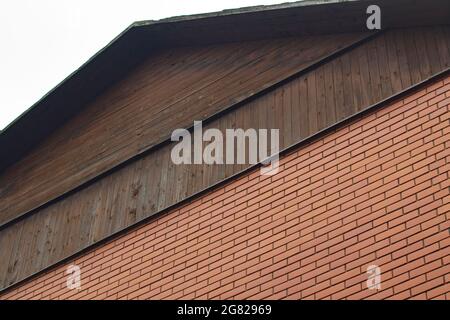 Maison en brique avec un toit en bois. Une maison de campagne dans le village. Le toit ressemble à du skate. L'élément architectural est un mur de briques. Banque D'Images