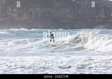 Australien en combinaison sur sa planche de surf surfant sur les vagues à une plage de Sydney par un jour hivernaux, Sydney, NSW, Australie Banque D'Images