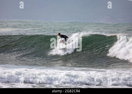 Australien en combinaison sur sa planche de surf surfant sur les vagues à une plage de Sydney par un jour hivernaux, Sydney, NSW, Australie Banque D'Images