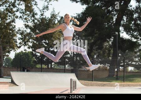 Une femme blonde atractive en bonne santé et en forme qui bonde à droite sur les obstacles du parc tout en regardant vers l'avant. Banque D'Images