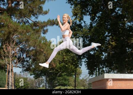 Une femme blonde atractive en bonne santé et en forme qui bonde à gauche sur les obstacles du parc tout en regardant vers l'avant. Banque D'Images