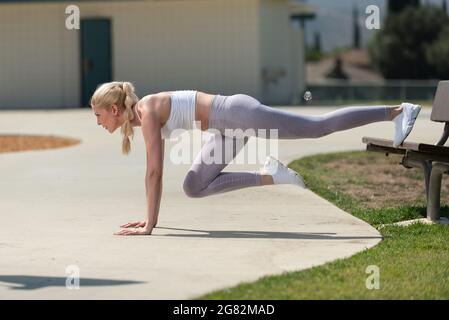 Une femme blonde atractive en bonne santé et en forme, qui fait un pont sur le trottoir du parc pour renforcer son cœur tout en regardant vers l'avant. Banque D'Images