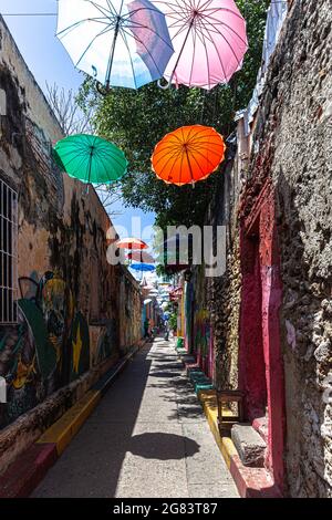 Rue étroite décorée de parasols colorés suspendus, Callejón Angosto, Barrio Getsemani, Cartagena de Indias, Colombie. Banque D'Images