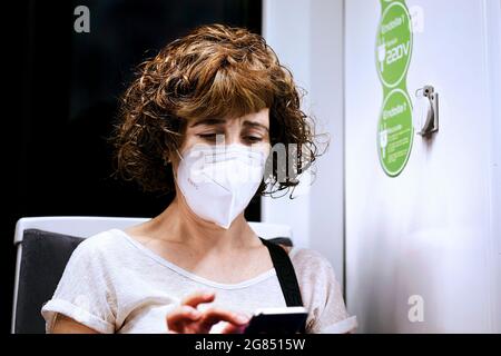 Une femme s'est assise dans un train portant un masque facial obligatoire, regardant son téléphone mobile, Barcelone, Espagne. Banque D'Images