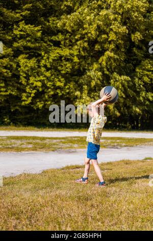 Une petite fille jouant avec le basket-ball par beau temps. Paysage rural avec arbres en arrière-plan. Banque D'Images