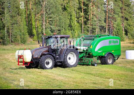 Agriculteur travaillant dans un champ de foin avec un tracteur Valtra et une enrubanneuse à ramasseuse-presse intégrée McHale 3 plus. Salo, Finlande. 28 août 2020. Banque D'Images