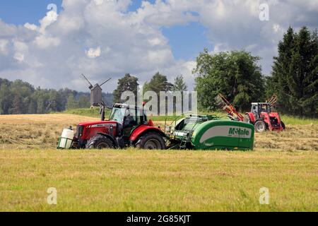 Tracteurs Massey-Ferguson dans le champ de foin avec enrubanneuse à ramasseuse-presse McHale et peigne rotatif pour la récolte de foin sec en été. Raasepori, Finlande. 25 juin 2021. Banque D'Images