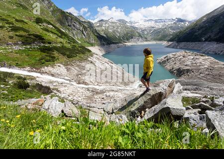 Garçon regardant sur le ruisseau alpin qui coule vers le lac réservoir de Kolnbreinsperre dans la vallée de Malte, Carinthie, Autriche Banque D'Images