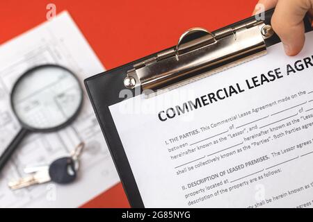 Man détient un contrat de location commercial en main. Presse-papiers avec document officiel. Arrière-plan avec des papiers immobiliers et la clé de maison Banque D'Images