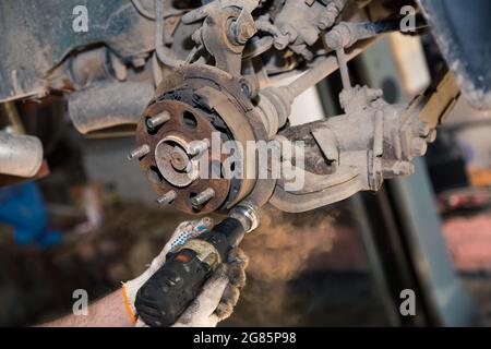 Les mains gantées utilisent un outil électrique pour nettoyer la rouille sur le moyeu de roue arrière. Dans le garage, un homme change de pièces sur un véhicule. Concept de petite entreprise, service de réparation et d'entretien de voiture. 4K UHD. Banque D'Images