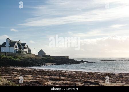 Rhosneigr, Anglesey, pays de Galles. Paysage d'hiver vue sur les falaises basses et une baie avec des vagues se brisant sur la plage. Bleu ciel et espace de copie. Banque D'Images