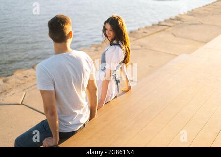 Vue de dessus de la jeune femme attrayante flirtant avec un homme assis sur le banc sur le front de mer de la ville près de la rivière dans la journée ensoleillée d'été. Banque D'Images