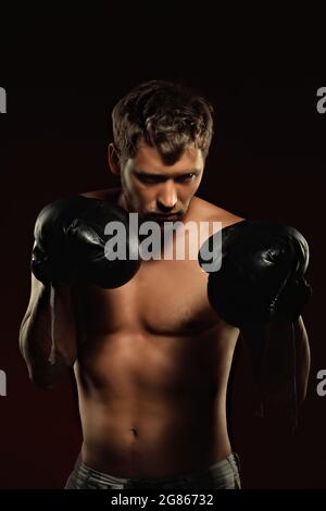 Voici un portrait spectaculaire d'un boxeur en vieux gants de boxe sur fond sombre. Un combattant athlétique des arts martiaux mixtes se tient en position de combat. Bannière pour les événements sportifs. Banque D'Images