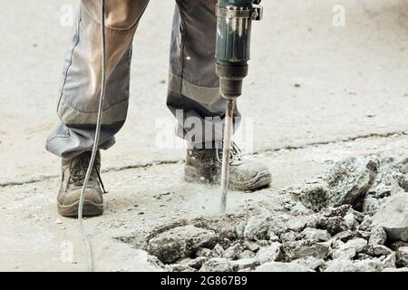 Un ouvrier répare la surface de la route avec un marteau à inertie le jour d'été. Travaux de construction sur la route. Arrière-plan industriel. Banque D'Images