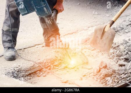 Un ouvrier répare la surface de la route avec un marteau à inertie le jour d'été. Travaux de construction sur la route. Arrière-plan industriel. Banque D'Images