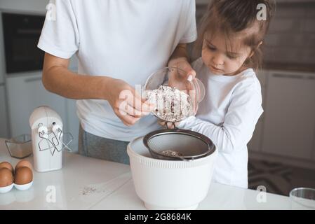 Jeune mère mélangeant de la pâte à gâteau avec petite fille fille fille à la table de cuisine à la maison. Maternité. Femme qui cuisine avec un petit tout-petit ensemble. Banque D'Images