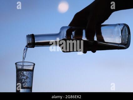 Potsdam, Allemagne. 14 juillet 2021. Un homme verse de la liqueur d'une petite bouteille dans un verre le soir. Dans le Brandebourg, selon l'Office d'État pour les questions de toxicomanie, les effets de la pandémie de Corona sont perceptibles par une augmentation notable des consultations dans les centres de conseil en toxicomanie de l'État. Credit: Soeren Stache/dpa-Zentralbild/ZB/dpa/Alay Live News Banque D'Images