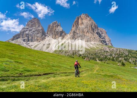 Jolie femme senior à cheval sur son vélo de montagne électrique en contrebas du sommet de Sassolungo dans les Dolomites de Selva Wolkenstein, Val Gardena, Tyrol du Sud Banque D'Images