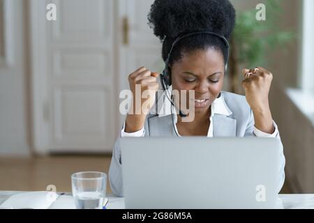 Une femme d'affaires africaine pleine de joie porte un casque enthousiaste lors d'un appel d'affaires en ligne avec un partenaire Banque D'Images