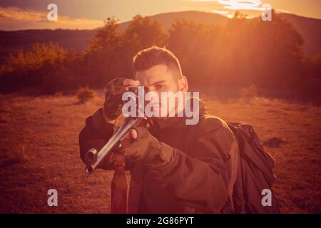 Chasseur avec fusil puissant avec animaux de repérage de portée. Fusil Hunter silhoueté dans beau coucher de soleil. Saison de chasse en automne. Banque D'Images