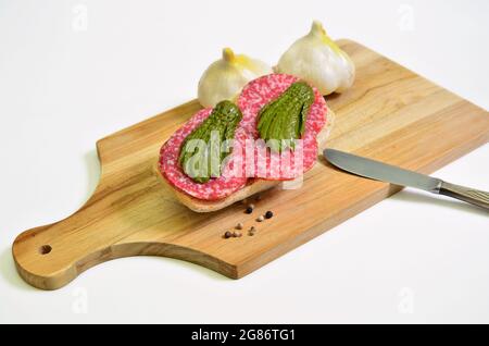 sandwich salami avec cornichon mariné et ail sur planche à découper, gros plan, isolé sur fond blanc Banque D'Images