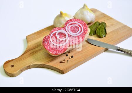 sandwich salami avec cornichons marinés, ail et rondelles d'oignon sur la planche à découper, gros plan, isolé sur fond blanc Banque D'Images