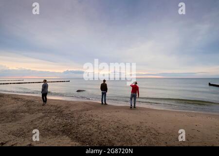 Trois personnes se retrouvant sur la rive de la mer d'Ost pendant le coucher du soleil nuageux Banque D'Images