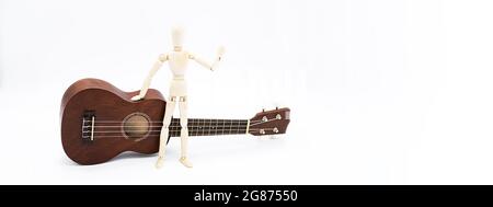 Ukulele guitare acoustique avec figure de mannequin humaine . Temps de pause pour le passe-temps. Art ou concept musical. Guitare hawaïenne brune et marionnette en bois Banque D'Images