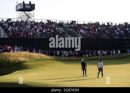 Le Collin Morikawa des États-Unis se pataise sur le 16e vert tandis que Louis Oosthuizen, d'Afrique du Sud, observe pendant la troisième journée de l'Open au Royal St George's Golf Club à Sandwich, dans le Kent. Date de la photo: Samedi 17 juillet 2021. Banque D'Images