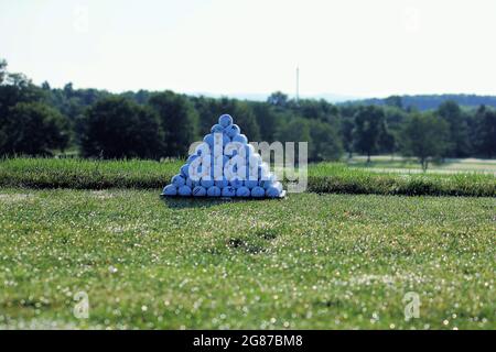 Une pyramide solitaire de balles de pratique de golf le matin contre un fond vert bordé d'arbre Banque D'Images