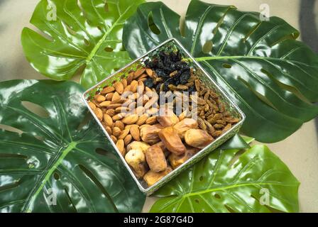 nourriture biologique saine dans un bol sur les feuilles tropicales, différents fruits secs amandes dattes secs raisins secs noirs d'or (kishmish) régime de jim Banque D'Images