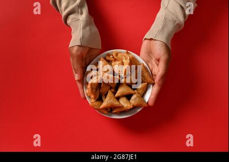 Mains tenant une délicieuse et douce assiette remplie de bonbons traditionnels marocains frais faits à la main, isolée sur fond rouge. Espace pour le texte. Tradi arabe Banque D'Images