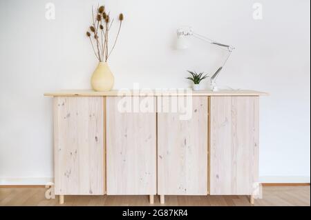 Panneau latéral en bois clair avec lampe et décoration de plantes contre un mur blanc, intérieur minimal et concept de maison avec espace de copie, mise au point sélectionnée Banque D'Images