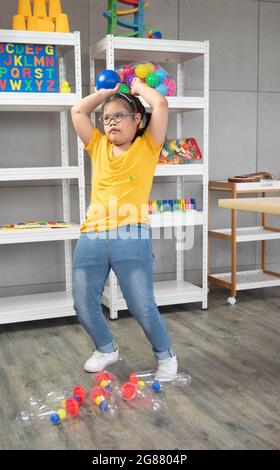 Une petite fille mignonne avec le syndrome de Down visant avant de lancer une balle en plastique à la cible tout en jouant à des jeux dans la salle de classe de l'enfant spécial. Banque D'Images