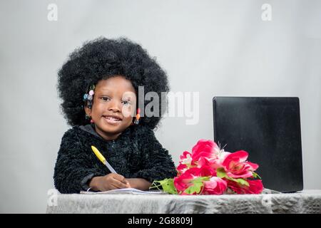 Fille africaine avec cheveux afro, écrire avec un stylo, étudier et rechercher l'excellence dans son éducation avec un ordinateur portable, fleur sur sa table Banque D'Images