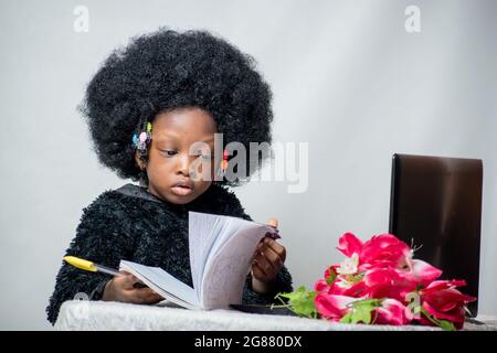 Fille africaine avec cheveux afro, écrire avec un stylo, étudier et rechercher l'excellence dans son éducation avec un ordinateur portable, fleur sur sa table Banque D'Images