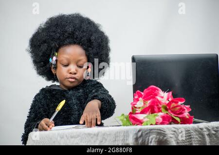 Fille africaine avec cheveux afro, écrire avec un stylo, étudier et rechercher l'excellence dans son éducation avec un ordinateur portable, fleur sur sa table Banque D'Images