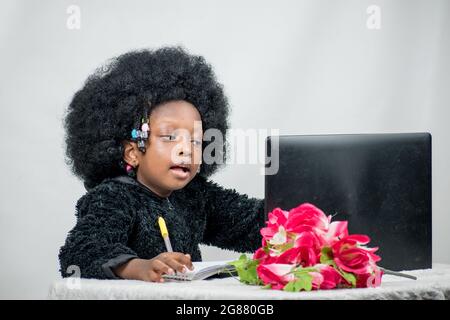 Fille africaine avec cheveux afro, écrire avec un stylo, étudier et rechercher l'excellence dans son éducation avec un ordinateur portable, fleur sur sa table Banque D'Images