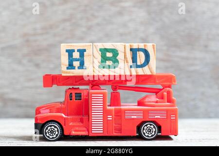 Camion d'incendie rouge tenir le bloc de lettres dans le mot HBD (abréviation de joyeux anniversaire) sur fond de bois Banque D'Images