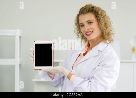 Jeune scientifique blond tenant un ordinateur de tablette à écran vide. Atmosphère de travail en laboratoire chimique. Banque D'Images