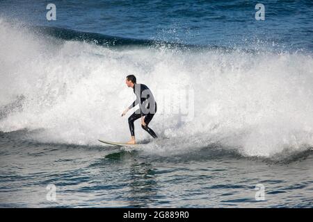 Australien en combinaison sur sa planche de surf surfant sur les vagues à une plage de Sydney par un jour hivernaux, Sydney, NSW, Australie Banque D'Images