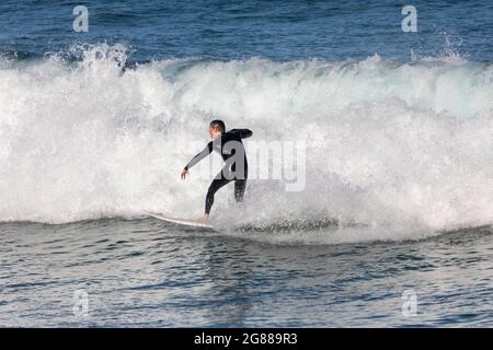 Australien en combinaison sur sa planche de surf surfant sur les vagues à une plage de Sydney par un jour hivernaux, Sydney, NSW, Australie Banque D'Images