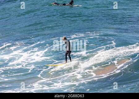 Australien en combinaison sur sa planche de surf surfant sur les vagues à une plage de Sydney par un jour hivernaux, Sydney, NSW, Australie Banque D'Images