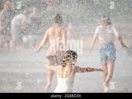 Les femmes et les filles marchent à travers la fontaine d'eau, vue à travers les pulvérisations et les gouttelettes, en été pendant la vague de chaleur Banque D'Images