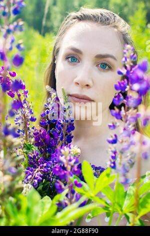 Belle jeune femme aux yeux bleus tenant un bouquet de lupins violets. Profiter de la nature et des fleurs. Fille romantique. Banque D'Images