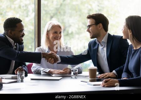 Des partenaires commerciaux très heureux et variés qui se contenent de passer la main sur la table Banque D'Images