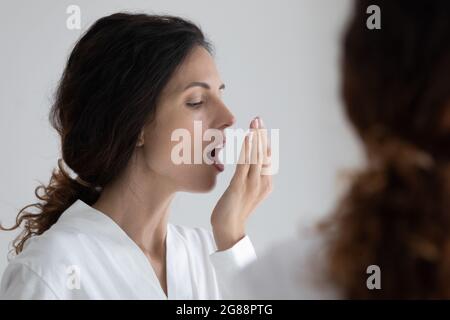 Jeune femme qui teste l'air qui sent l'haleine en tenant la paume par les lèvres Banque D'Images