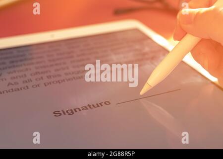 La main féminine tient le crayon de stylet et met une signature électronique en contrat sur la tablette, photo sélective de mise au point Banque D'Images