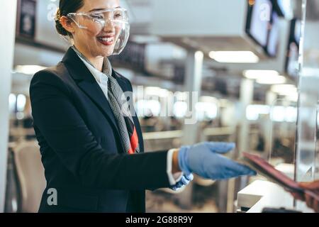 Le personnel féminin de l'aéroport porte un masque de protection pour aider les voyageurs. Femme travaillant au comptoir d'enregistrement de la compagnie aérienne pendant une pandémie. Banque D'Images