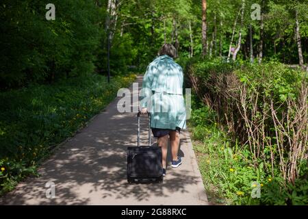 Une femme porte un chariot sur le chemin. Une femme d'âge porte des choses sur le chemin. La fille rentre à la maison dans le parc. Banque D'Images